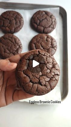 a person is holding a chocolate cookie in front of some cookies on a baking sheet