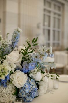 a bouquet of blue and white flowers sitting on top of a table next to wine glasses