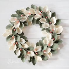 a white wreath with green leaves and pink berries on the front is hung on a wall