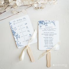 two wedding programs with ribbons tied to them on a white surface next to dried flowers