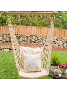 a hammock chair with pillows on it in the grass next to a potted plant