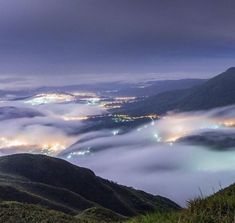 fog covers the mountains and valleys at night with lights in the distance, from an overlook point