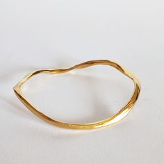 Irregular golden bracelet.   Its modern design makes it a perfect gift for strong woman. This wavy bangle is made of an  hypoallergenic alloy and golden plated (10 micron) to give its polished shiny look.  I made it in my Spain workshop with high quality materials which ensures a perfect finish with great durability. It is an easy wear piece of jewelry that you can rock both with jeans or a cocktail dress.  This stackable bracelet is also available in yellow gold and pink gold. SIZING: --------- Elegant Stackable Brass Bangle, Brass Bangle Bracelet For Everyday Wear, Modern Brass Bangle For Everyday Wear, Handmade Bangle For Everyday Use, Handmade Everyday Bangle, Minimalist Bangle Bracelet As Gift For Her, Elegant Hammered Brass Bangle, Handmade Gold Cuff Bracelet For Everyday, Minimalist Gold Cuff Bracelet