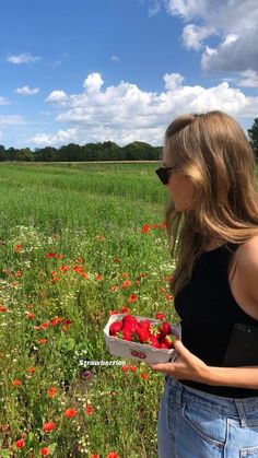 a woman standing in a field holding a basket of strawberries