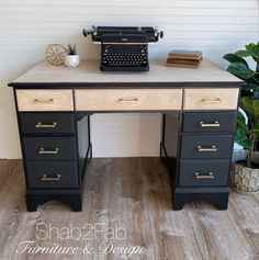 a black and white desk with a typewriter on it's top next to a potted plant