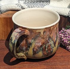 a coffee mug sitting on top of a wooden table next to flowers and a blanket