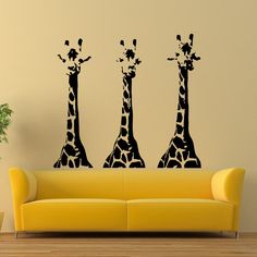 three giraffes standing next to each other on a wall in a living room