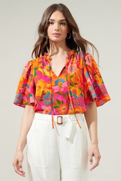 Rock this groovy floral print wherever you go. The Idalia floral print features multi-colored boho florals against a vibrant orange-ground. It decorates the Dupont top, a split neckline with short flouncy sleeves. It maintains a relaxed fit and can be tied at the neck and tucked into high waisted linen pants.- Flouncy sleeves- Split neckline- Ruffle trim- Relaxed fit- Color: Orange FloralSize + Fit - Model is 5'9" and wearing size S- Measurements taken from size S - Chest: 19 1/2"- Length: 25" F Colorful Tops Outfit, Vibrant Casual Outfits, Groovy Outfit Women, Printed Tops Designs, Orange Top Outfit, Floral Shirt Outfit, Flouncy Sleeves, High Waisted Linen Pants