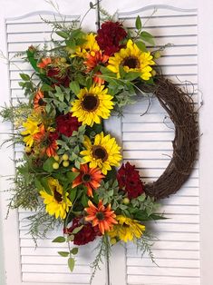 a wreath with sunflowers and other flowers is hanging on the front door's shutter