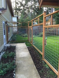 a fenced in backyard area with grass and plants on the side of the house