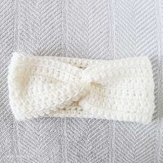 a white knitted headband laying on top of a gray and white bed sheet