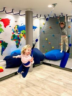 two children are playing in an indoor climbing area with blue balls and ropes, while one child is jumping on the wall