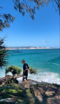 a man standing on top of a lush green hillside next to the ocean