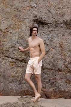 a shirtless man standing in front of a rock wall with his hand on his hip