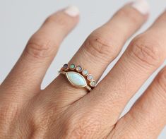 a woman's hand wearing a ring with an oval shaped opal and multi colored stones