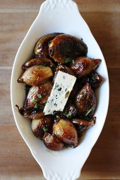 a white bowl filled with roasted potatoes and topped with parmesan cheese on a wooden table