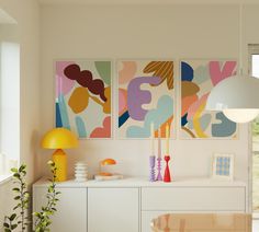 three paintings hang on the wall above a white cabinet in a room with yellow accents