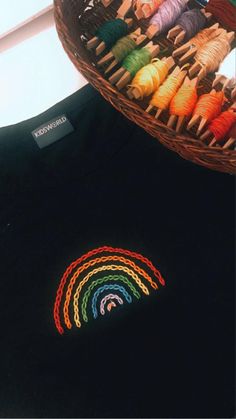 a basket filled with different colored thread next to a t - shirt that has a rainbow embroidered on it