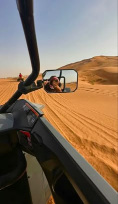 there is a person in the side mirror of a vehicle driving through sand dunes on a sunny day