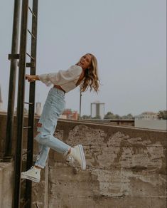 a woman standing on top of a metal pole next to a cement wall and ladder