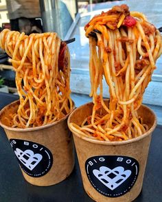 two cups filled with noodles and meat on top of a table next to each other