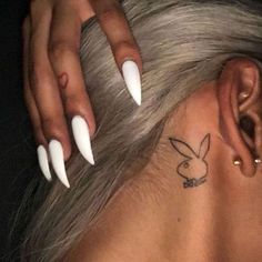 a woman's ear with white acrylic nails and a bunny ears tattoo