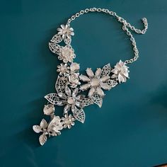 a silver necklace with flowers and leaves on a blue background, hanging from a chain