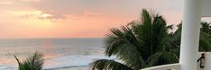 the sun is setting over the ocean with palm trees on the balcony and in the foreground