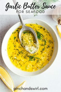 garlic butter sauce for seafood in a white bowl with a spoon and lemon wedges