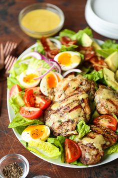 a plate with chicken, lettuce and tomatoes on it next to some dressing