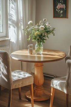 a small round table with two chairs around it and a vase filled with flowers on top