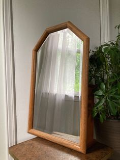 a wooden mirror sitting on top of a table next to a potted plant and window