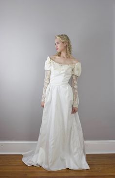 a woman in a white wedding dress standing on a wooden floor with her hands behind her back