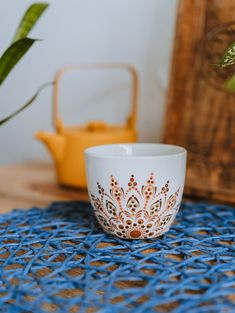 a white cup sitting on top of a blue tablecloth next to a potted plant