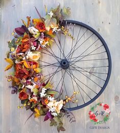 an old bicycle wheel decorated with flowers and greenery on the side of a wooden wall