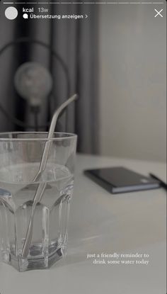 a glass with two spoons in it sitting on a table next to a cell phone