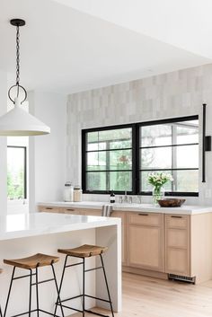 a kitchen with white counter tops and wooden stools next to an island in front of two windows