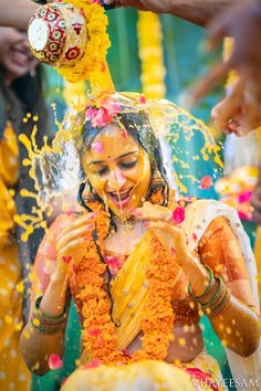 a woman covered in orange and yellow powder throwing confetti on her face as she smiles