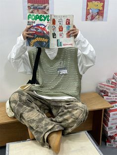 a man is sitting on a bench reading a book while wearing camo pants and a white shirt