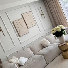 a living room with white couches and paintings on the wall above them, along with a vase filled with flowers