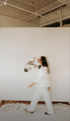 a woman standing in front of a white wall with pictures on the wall behind her