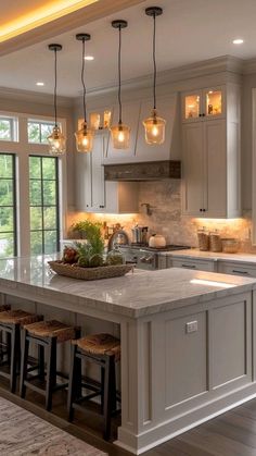 a large kitchen island with stools in front of it and lights hanging from the ceiling