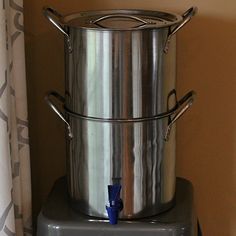 two large metal containers sitting on top of a counter next to a window with curtains