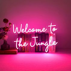 a pink neon sign that says welcome to the jungle on top of a stack of books