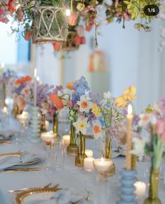 a long table with flowers and candles in vases on top of it, along with other place settings