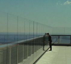 a man standing on top of a glass walkway next to the ocean in front of him