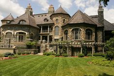 a large stone house with lots of windows on the front and side of it, surrounded by lush green grass