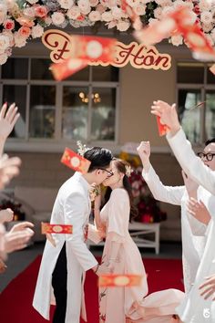 a group of people that are standing in front of a red and white arch with flowers on it