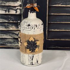 a white bottle with burlap and flowers on it