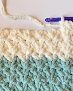 the crochet pattern is being worked on by someone using a blue handled knitting needle